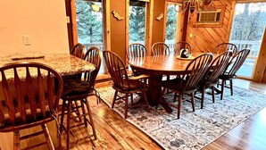 Un comedor de madera con una mesa redonda y sillas, ventanas amplias y una araña.