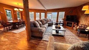 Una sala de estar acogedora con un sofá modular, una mesa de comedor y sillas. Hay un televisor y una chimenea.