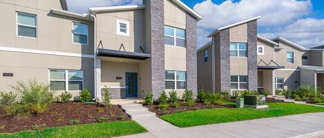 A modern multi-story residential building with a flat roof, large windows, and a well-maintained lawn.