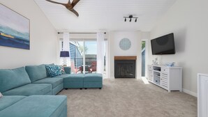 Una sala de estar con un sofá modular, una chimenea, un televisor y un ventilador de techo.
