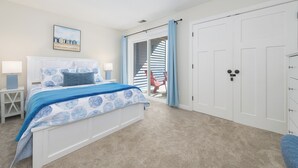 Un dormitorio con cama, mesita de noche, una silla, armario y puerta que da a un balcón.