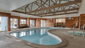 Una piscina interior con paredes y vigas de techo de madera, rodeada de sillones y mesas.