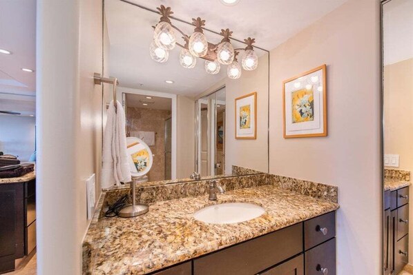 Une salle de bain avec un lavabo doté d’un plan de travail en granit, un miroir et un luminaire placé au-dessus.