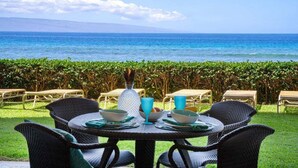Un espace de restauration en plein air, avec des chaises et des tables en osier, offrant une vue sur une mer d’un bleu profond et sur une chaîne de montagnes lointaine.