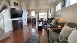 A spacious living room with a large flat-screen TV, a sofa, a coffee table, and a dining area with a table and chairs.