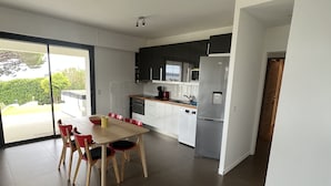 A modern kitchen with a dining area, featuring a large table and chairs, a refrigerator, and a view through the glass door. - Ground floor villa with private pool (Cavalaire-sur-Mer)
