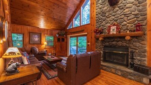 Interior acogedor de una cabaña con chimenea de piedra, paredes de madera y un sofá de cuero.