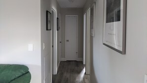 Ein schmaler Korridor mit Holzboden, weißen Wänden und gerahmten Bildern an den Wänden.