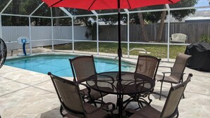 Ein überdachter Außenbereich mit Pool, Terrassenmöbeln und einem roten Sonnenschirm.