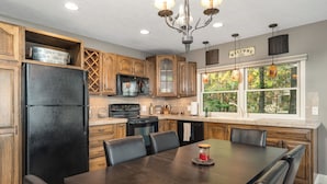 A kitchen with wooden cabinets, a black refrigerator, a dining table with chairs, and a window with a view of trees. - Northern Tranquility on Black Lake
Available the weeks of July 11 and July 18!!! (Cheboygan)