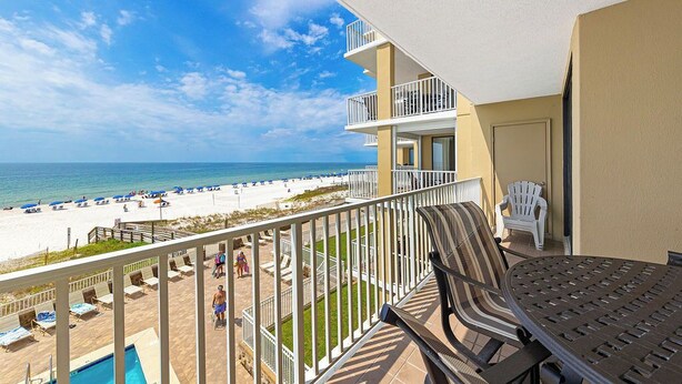 A balcony with a view of a beach and ocean, a pool, and outdoor seating.