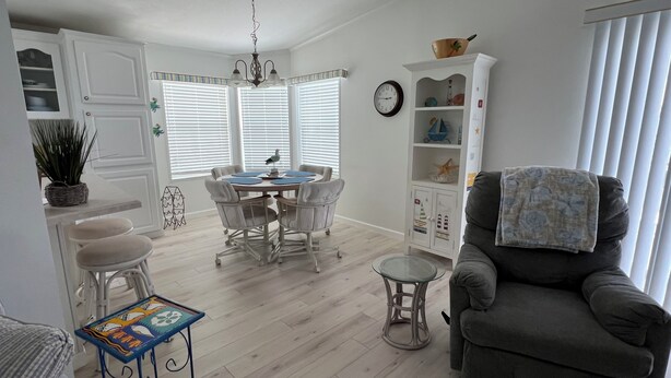 A dining area with a round table and chairs, a kitchen with white cabinets, and a living area with a sofa and a clock on the wall.