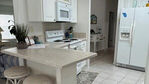 A kitchen with white cabinetry, a central island with stools, a microwave, and a refrigerator.