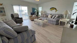 A living room with a sofa, armchair, and coffee table. There is a fish decoration on the wall and a lamp on a side table.