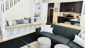 A modern living room with a grey sofa, ottomans, and a white staircase. - Ski in/out Disciples Boyne Moun. All Seasons Suite (Boyne Falls)