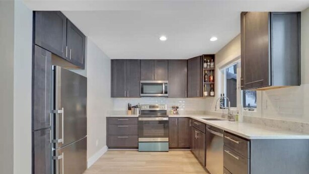 A modern kitchen with dark cabinetry, stainless steel appliances, and a light-colored countertop. - Ski in/out Disciples Boyne Moun. All Seasons Suite (Boyne Falls)