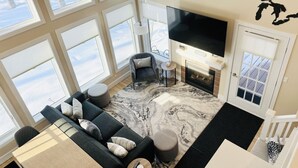 A modern living room with a fireplace, large windows, a flat-screen TV, and a cozy seating area. - Ski in/out Disciples Boyne Moun. All Seasons Suite (Boyne Falls)