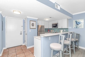 Una cocina con un refrigerador blanco, un microondas y un lavamanos. Hay tres taburetes de bar y una pequeña isla con un lavamanos.