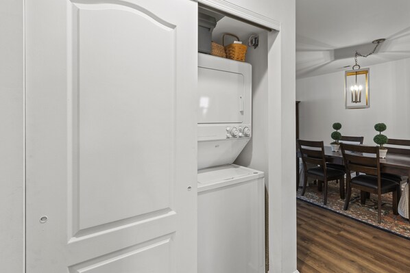 A white wardrobe with a basket on top, a wooden dining table with chairs, and a hanging light fixture. - Escape to Robin's Nest! (Lewes)