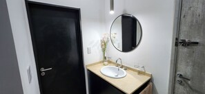 Un baño con un lavamanos blanco, un espejo redondo y una puerta negra.