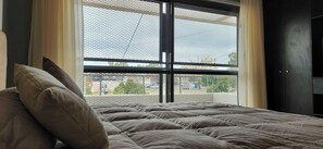 Una cama con cabecera, una ventana con mosquitera y un armario de color oscuro.