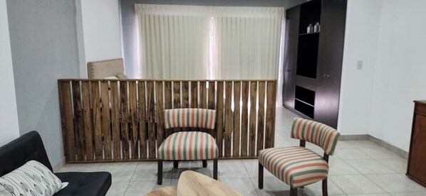 Una sala de estar con un separador de madera, dos sillones a rayas, un sofá y un mueble para televisión.