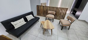 Una sala de estar con un sofá negro, dos sillones a rayas, una mesa de centro de madera y un separador de madera.