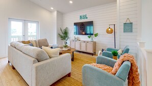Ein modernes Wohnzimmer mit einer Couch, Sesseln, einem Couchtisch und einem an der Wand befestigten Fernseher.