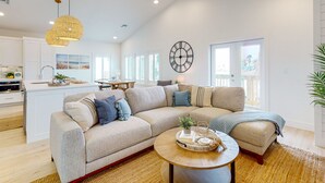 Ein großzügiges Wohnzimmer mit einer großen, abgewinkelten Eckcouch, einem runden Couchtisch und einer Küche im Hintergrund.