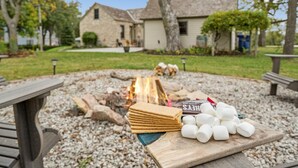 A picnic setup with a fire, marshmallows, and chocolate bars on a wooden table in a park area with stone buildings in the background. - The Rock House • Historic Stone Cottage • Walk to Central (Pella)