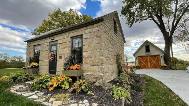 A stone house with a garage, surrounded by autumn foliage and a large tree. - The Rock House • Historic Stone Cottage • Walk to Central (Pella)