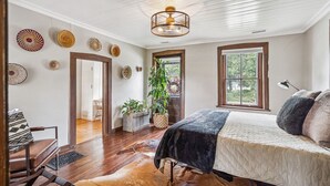 A bedroom with a bed, a window, a plant, and a door leading to another room. - The Rock House • Historic Stone Cottage • Walk to Central (Pella)