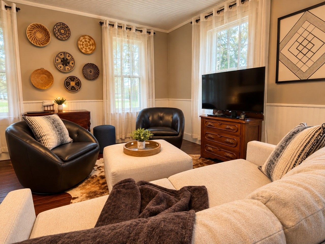 Ein Wohnzimmer mit einem schwarzen Ledersofa, einem beigefarbenen Sofa, einem Couchtisch, einem Fernseher und dekorativen Tellern an der Wand.