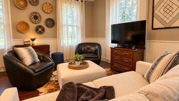 Ein Wohnzimmer mit einem schwarzen Ledersofa, einem beigefarbenen Sofa, einem Couchtisch, einem Fernseher und dekorativen Tellern an der Wand.