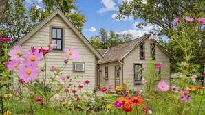 A two-story house surrounded by a garden with various flowers. - The Rock House • Historic Stone Cottage • Walk to Central (Pella)