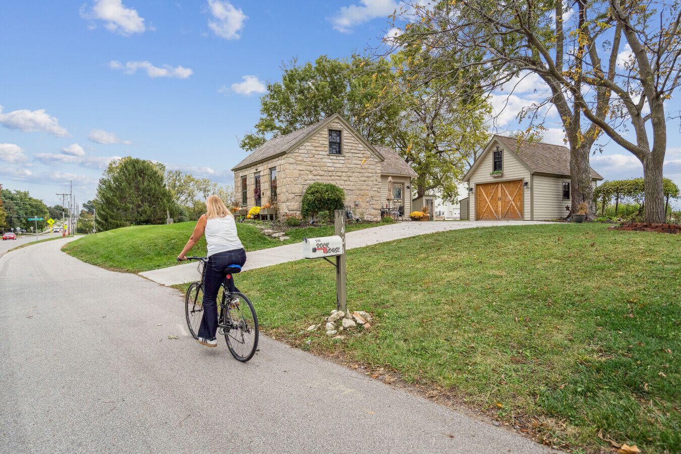 Una calle residencial con una casa de piedra, un buzón y un ciclista.