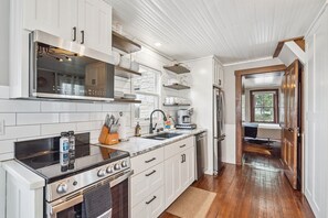 A modern kitchen with white cabinetry, stainless steel appliances, and a wooden floor. - The Rock House • Historic Stone Cottage • Walk to Central (Pella)