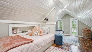 A cozy attic bedroom with a loft bed, a small seating area, and a large window offering a view of the outdoors.