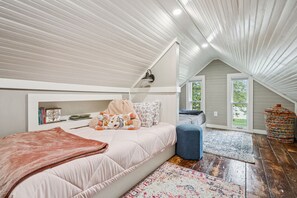 A cozy attic bedroom with a loft bed, a small seating area, and a large window offering a view of the outdoors. - The Rock House • Historic Stone Cottage • Walk to Central (Pella)