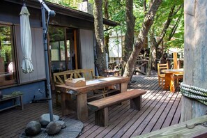 Une terrasse en bois avec une table et des bancs, entourée d’arbres.