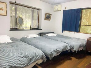 Une chambre avec deux lits simples, une fenêtre avec des rideaux bleus, une horloge murale et un tableau encadré.