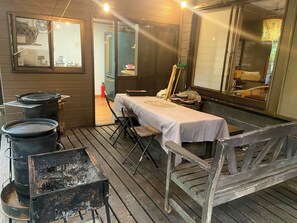 Un espace de restauration en plein air au style rustique, avec une table et des bancs en bois, entouré de grands tonneaux noirs et d’un barbecue en métal.