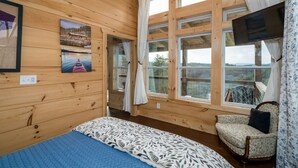 Una habitación tipo cabaña de madera con una cama, una silla y ventanas grandes.