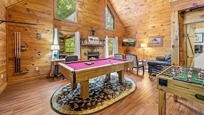Un espacio acogedor con piso de madera, mesa de billar, mesa de fútbol de mesa y chimenea.
