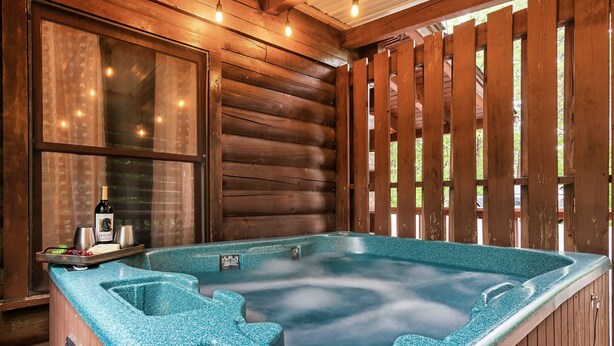 Un jacuzzi con revestimiento de madera, una ventana con cortinas y una botella de champán sobre una bandeja.