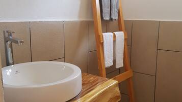 A bathroom with a wooden vanity, a white sink, a wooden towel rack, and a toilet.