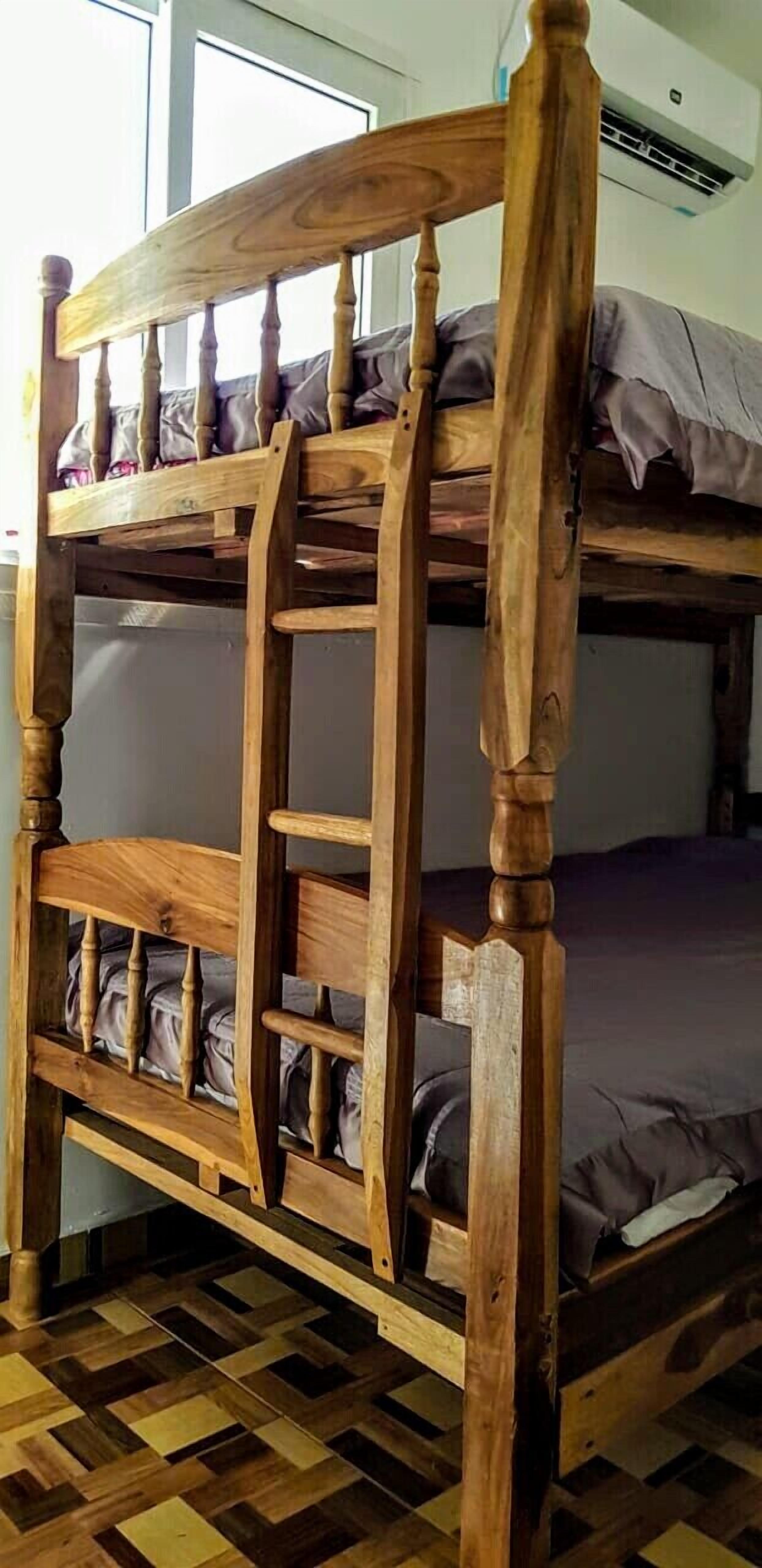 Una cama litera de madera con escalera, suelo a cuadros y una ventana al fondo.