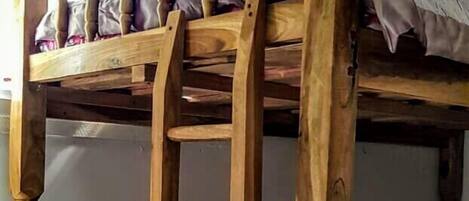 Una cama litera de madera con escalera, suelo a cuadros y una ventana al fondo.