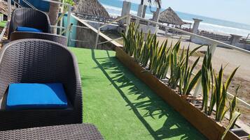 En patio ved stranden med fletstole og en bindingsværksbygning.