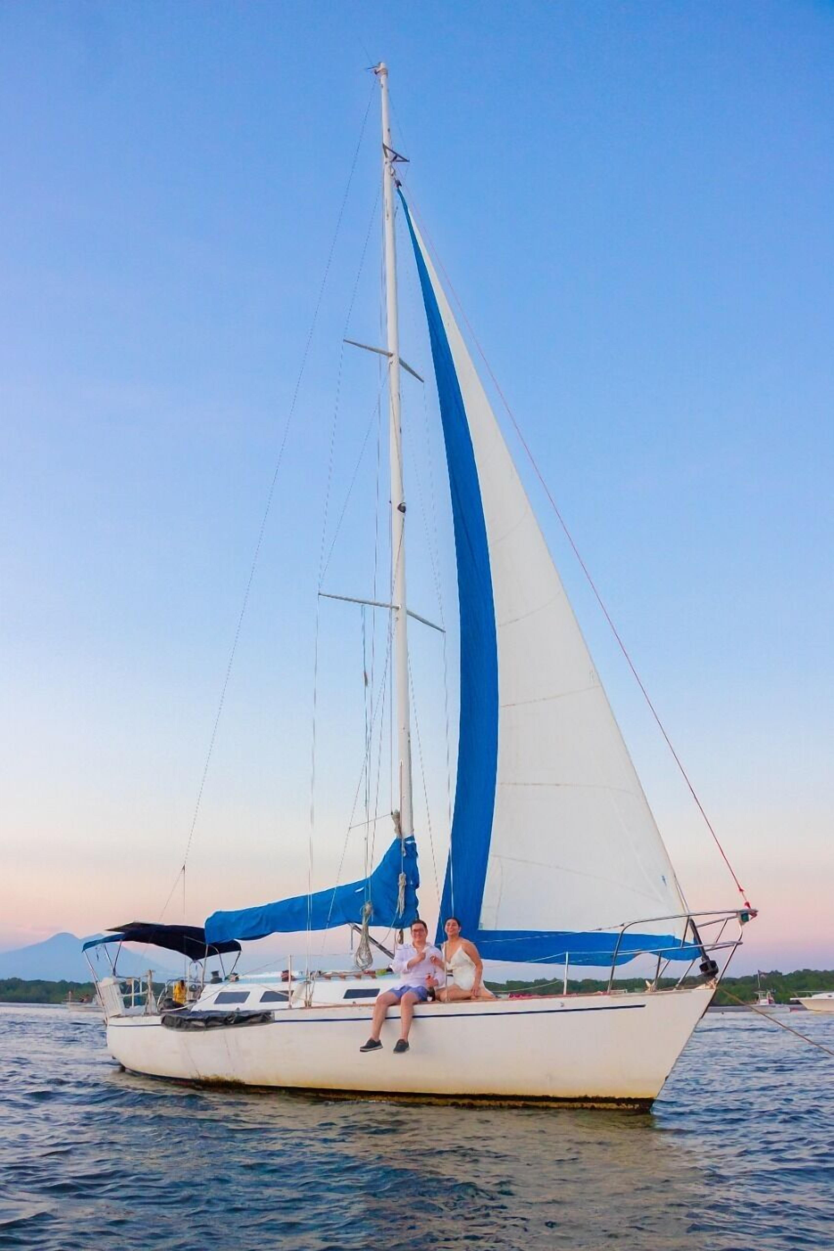 Eine Segelyacht mit zwei Personen an Bord, bewölkter Himmel und ruhiges Wasser.